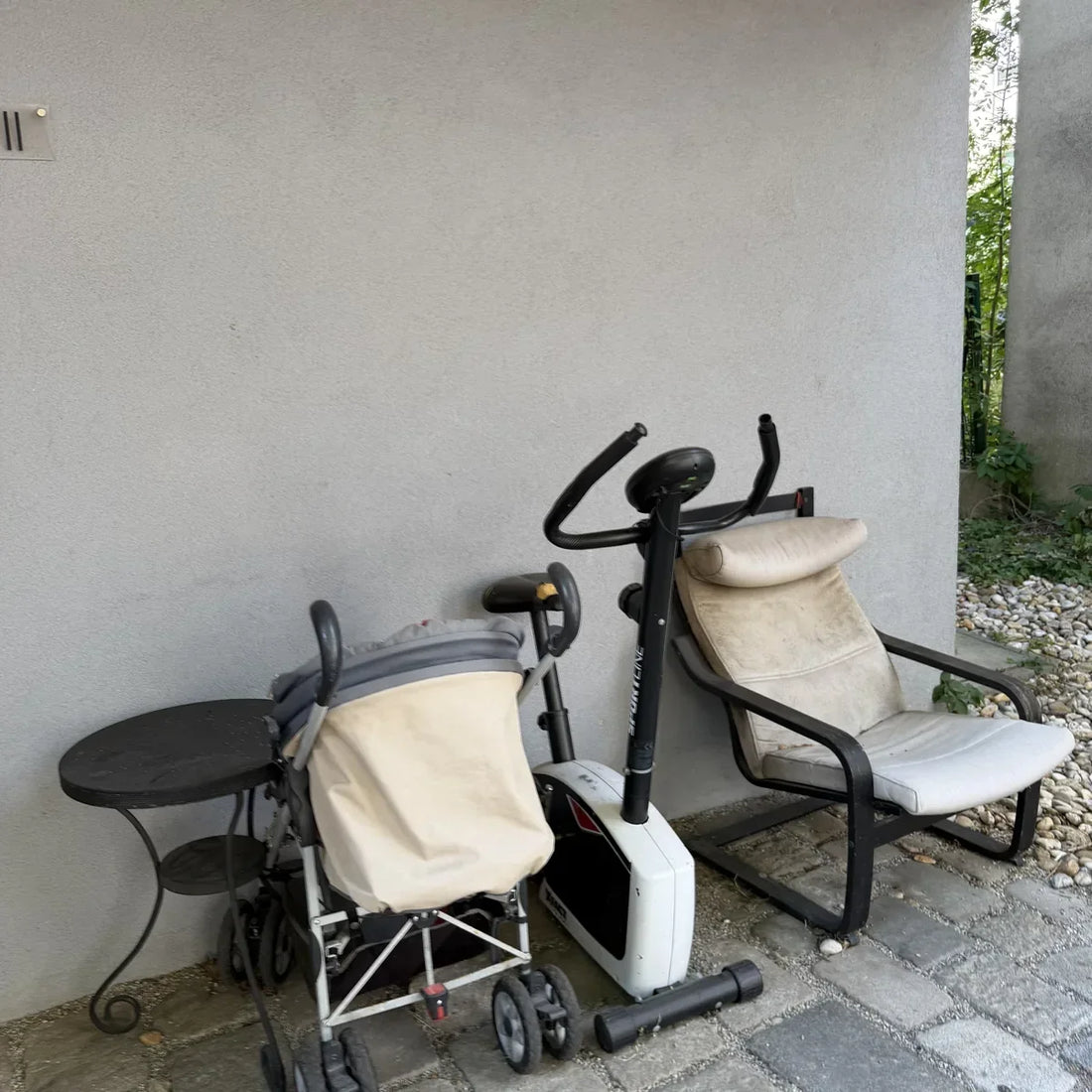 Kinderwagen, Crosstrainer und ein Sessel abgestellt an einer Hauswand im Innenhof